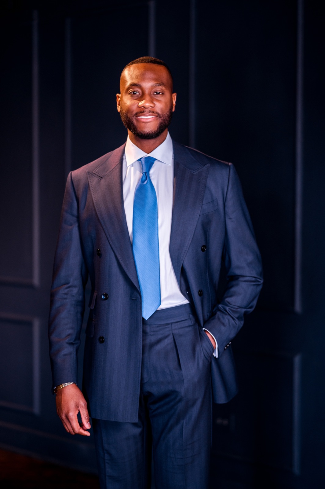 George Oginni portrait, navy suit on dark paneling